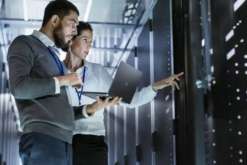 Male IT Specialist Holds Laptop and Discusses Work with Female Server Technician.